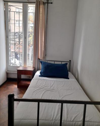 a bed with a blue pillow in a room with a window at Atacama Hostel Backpackers in Santiago