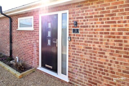 a red brick house with a black door at Bright & Stylish Bungalow Retreat in Attleborough in Attleborough