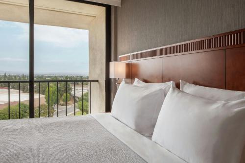 a bedroom with a bed with white pillows and a balcony at Courtyard by Marriott Los Angeles Pasadena/Monrovia in Monrovia