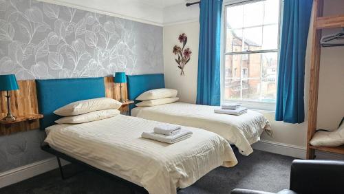 two beds in a room with blue curtains and a window at Edward Hotel in Gloucester