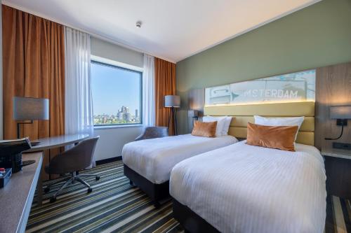 a hotel room with two beds and a desk at Leonardo Royal Hotel Amsterdam in Amsterdam