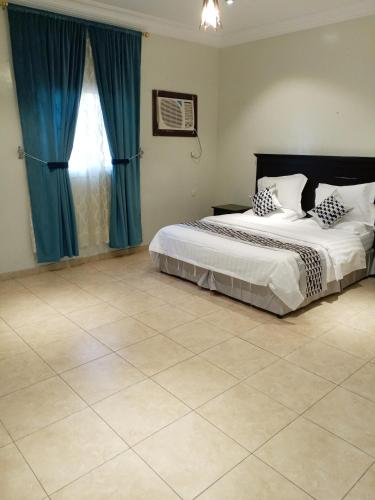 a bedroom with two beds with blue curtains and a tile floor at أجنحة أجواء إيلاف الاولى in Taif