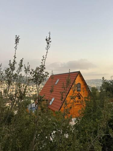 eine orangefarbene Scheune mit rotem Dach auf einem Hügel in der Unterkunft أكواخ المها oryx cottage in Adschlun