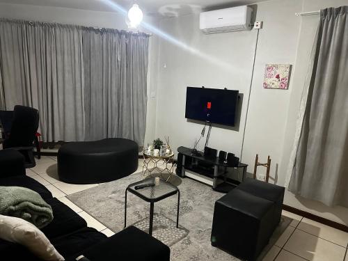 a living room with a couch and a flat screen tv at Feel At Home Cosy Apartment in Gaborone
