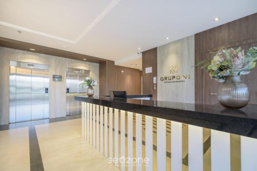a lobby with a reception counter and a vase with flowers at MHFs - Apts Variados em Prédio com Vista para o Mar em Itapema in Itapema