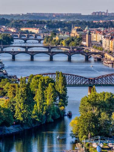 a bridge over a river with trees and a city at Glamping Escape Prague with Hot Tub and Vysehrad Castle View in Prague