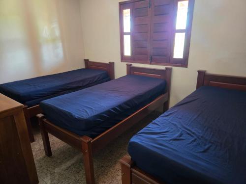 a room with three beds with blue sheets and a window at Casa de Campo Ibicoara in Ibicoara