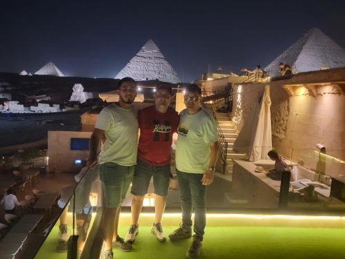 three men standing in front of the pyramids at night at Inside Pyramids Inn in Banī Ghālib