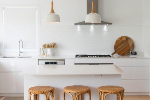a kitchen with white counters and stools at Biirinba in Yamba