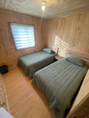 Dos camas en una habitación pequeña con paredes de madera. en Cabañas de campo, en Angol