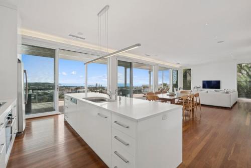 a kitchen with white cabinets and a dining room with a table at Coastal Panorama - Spectacular Views, Sleeps 8 in Coffs Harbour