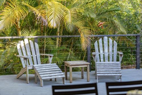 two white chairs and a stool on a deck with palm trees at Lizzie Bliss in Elizabeth Beach