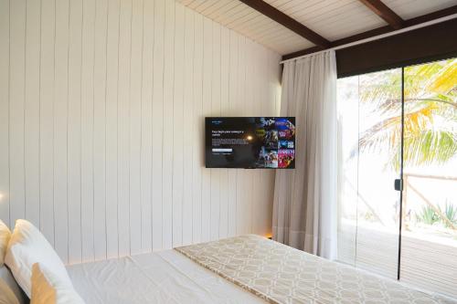a bedroom with a bed with a tv on the wall at Vila Corada in Pipa