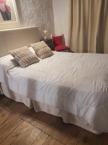 a white bed with two pillows and a red chair at Perla Gris Chascomus Departamento a 3 cuadras de la laguna y 4 del centro in Chascomús