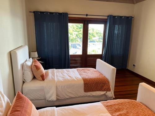 a bedroom with two beds with blue curtains and a window at Vashays Caribbean Hideaway in Freetown Village