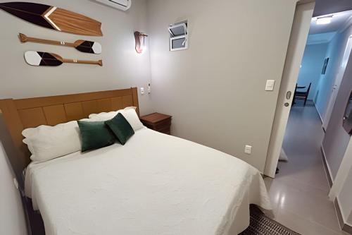 a bedroom with a bed with white sheets and green pillows at Melhor local de Pitangueiras com serviço de praia in Guarujá