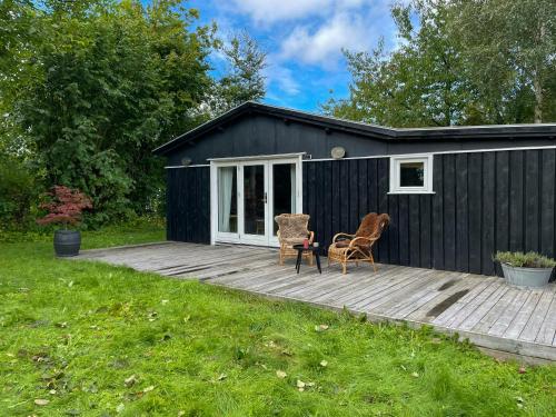 a black shed with two chairs on a wooden deck at Holiday Home Near Tisvilde Forest And Rhubarb Farm in Vejby Strand