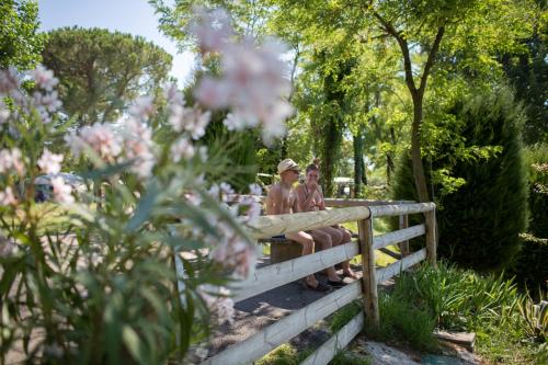two people sitting on a fence in a garden at Camping Fossalta in Lazise