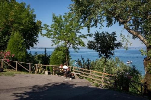 two people sitting on a bench near the water at Camping Fossalta in Lazise