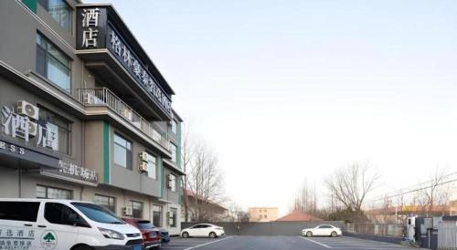 a building with cars parked in a parking lot at GreenTree Inn Express Qingdao Jiaodong International Airport in Qingdao