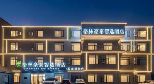 a lit up building with cars parked in front of it at GreenTree Inn Express Qingdao Jiaodong International Airport in Qingdao