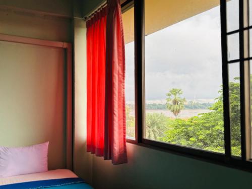 a bedroom with a window with red curtains at โรงแรมรอยัลจอมมณี เฮอริเทจ in Ban Na Kai