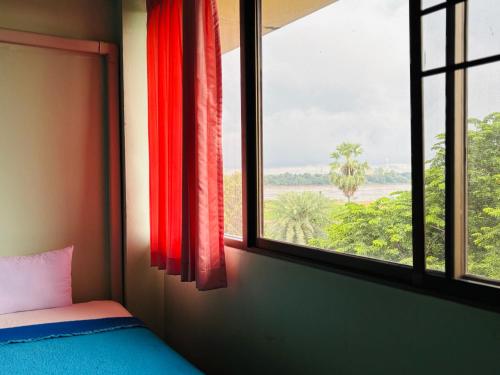 a room with a bed and a window with red curtains at โรงแรมรอยัลจอมมณี เฮอริเทจ in Ban Na Kai