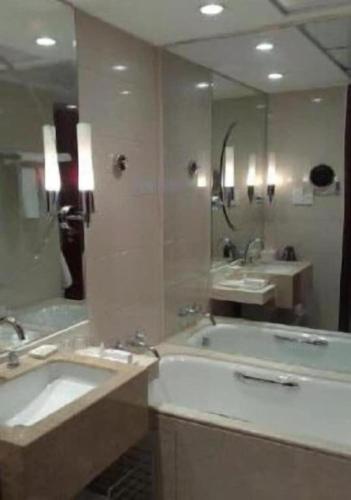 a bathroom with two sinks and a tub and a mirror at New Century Grand Hotel Zhuji Yaojiang in Shaoxing
