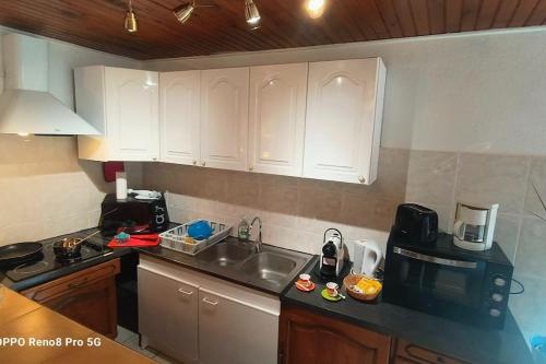 a kitchen with white cabinets and a sink and a microwave at La chacuniere in Saint-Amant-Tallende