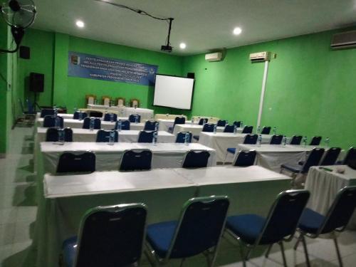 a conference room with white tables and chairs and a screen at Four Hostel Bandar Lampung in Tanjungkarang