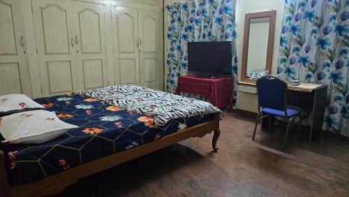 a bedroom with a bed and a desk and a television at Eden Garden Homestay in Mysore