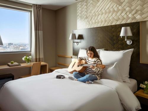 a woman sitting on a bed playing a guitar at ibis Jeddah City Center in Jeddah