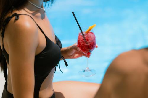 a woman in a black bikini holding a drink at Hotel Riva Del Sole in Giovinazzo