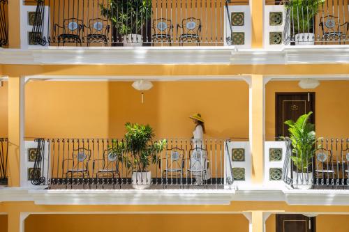 a woman standing on the balcony of a building at Soleil by Soluna - A Charming Touch of Hoi An Heritage - formerly Hoi An Babylon Luxury Hotel in Hoi An