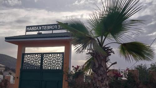 a palm tree next to a building with a sign at Gîte Forest Kasbah in Timsal