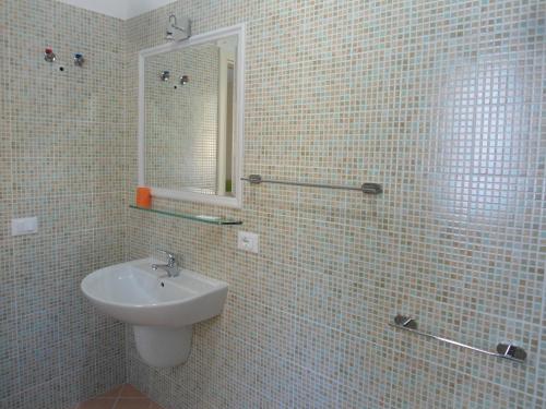 ein weiß gefliestes Bad mit einem Waschbecken und einem Spiegel in der Unterkunft Appartamento Bilocale a 200 m dalla spiaggia in Vieste