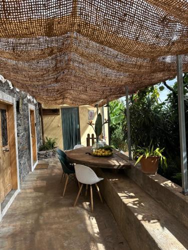 eine Terrasse mit einem Tisch und Stühlen unter einem Strohschirm in der Unterkunft Casa de basalto in Caniço