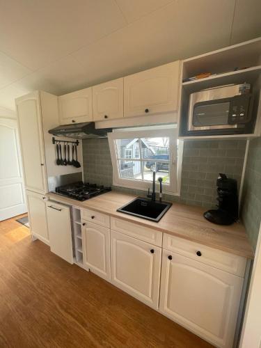 a kitchen with white cabinets and a sink and a window at Chalet VeerLake in Lathum