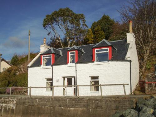 a white house with a black roof and red windows at Fleet Cottage in Portree