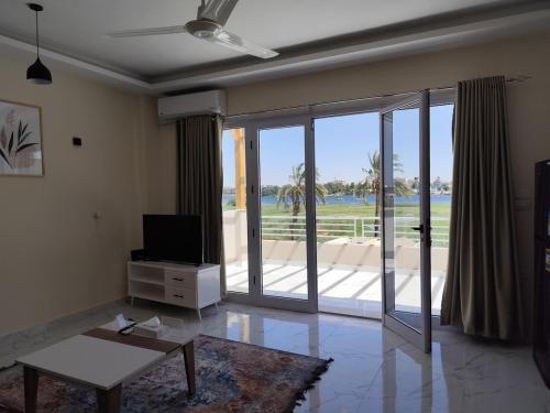 a living room with a tv and a sliding glass door at Royal Nile Villa - Luxury Nile Sky Penthouse 2 in Al Aqālitah