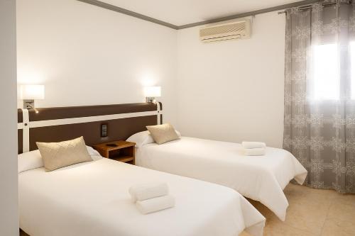 a room with two beds with white sheets and a window at HOSTAL LAS PALOMAS in Lucena