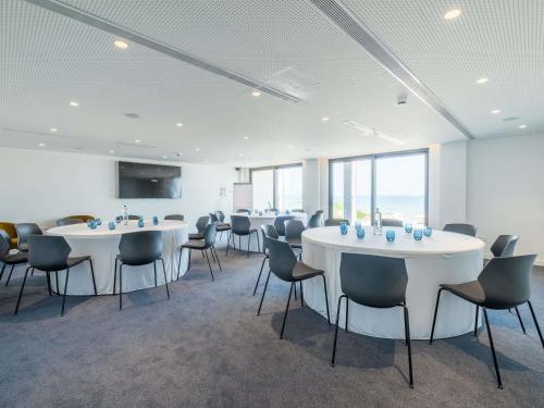 a room with white tables and chairs and windows at Mercure Larnaca Beach Resort in Larnaka