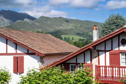 a house with a roof with mountains in the background at Logis Hôtel Baratxartea in Sare