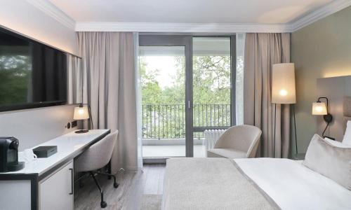 a hotel room with a bed and a desk and a balcony at Leonardo Hotel Hannover in Hannover