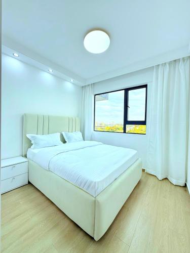 a white bedroom with a large bed and a window at Pearl Luxe Homes at Orchid Residency - Spacious 2BR in Westlands With Pool, Gym, Rooftop views & breakfast café in Nairobi