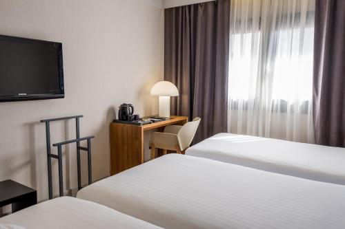 a hotel room with two beds and a desk with a television at Zenit Abeba in Madrid