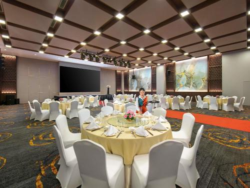 a conference room with tables and white chairs and a presenter at Mövenpick Living West Hanoi in Hanoi
