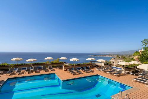 a swimming pool with chairs and umbrellas and the ocean at Eurostars Monte Tauro in Taormina