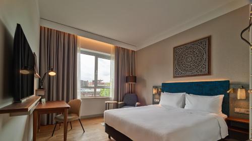 a hotel room with a bed and a desk and a window at voco The Hague by IHG in The Hague