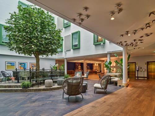 a lobby with chairs and tables and a tree at voco The Hague by IHG in The Hague